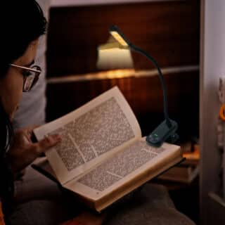 Lampe de Lecture Flexible et Réglable en Plastique accrochée à un livre dans les mains d'une personne sur fond marron