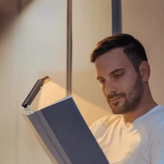 Lampe de Lecture LED Portable avec Luminosité Réglable sur un livre avec un homme qui lit sur fond beige